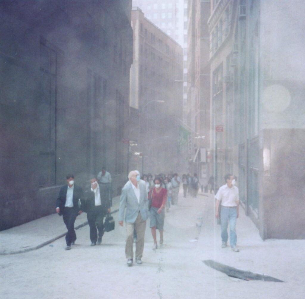 A dust-filled city street with people walking through a hazy, debris-covered environment, some wearing masks and business attire as they move between tall buildings.